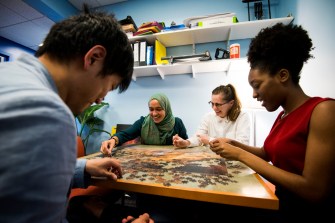 Four people sit around a table working together on a jigsaw puzzle.