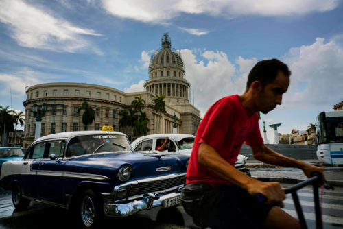 FILE - In this July 15, 2016 file photo, a man cycles alongside taxi drivers near the Capitol building in Havana, Cuba. A rare poll of Cuban public opinion taken in late 2016 has found that most Cubans approve of normal relations with the United States and large majorities want more tourism and private business ownership.  (AP Photo/Ramon Espinosa, File)