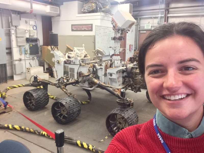 Carly Parlato, standing with a replica of the Mars rover Curiosity behind her, while on co-op at the NASA Jet Propulsion Laboratory