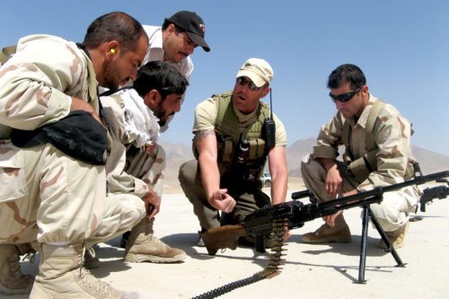 In this August 2007 photo, Phil McTigue (second from right) shows members of the National Interdiction Unit, a specialized counter narcotics law enforcement unit in Afghanistan, how to use a Russian PKM machine gun. The weapons were used by the unit for operations and raids on narcotics compounds throughout the country. Photo courtesy of Phil McTigue.
