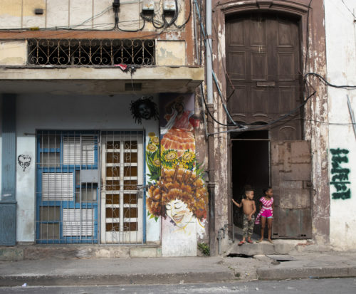 Two kids stand outside a crumbling doorway flanked by graffiti. Photo by Adee Peer