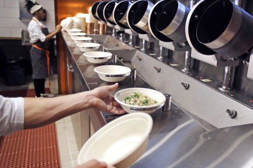In this May 3, 2018, file photo a worker lifts a lunch bowl off the production line at Spyce, a restaurant which uses a robotic cooking process, in Boston. Robots aren’t replacing everyone, but a quarter of U.S. jobs will be severely disrupted as artificial intelligence accelerates the automation of today’s work, according to a new Brookings Institution report published Thursday, Jan. 24, 2019. (AP Photo/Charles Krupa, File)