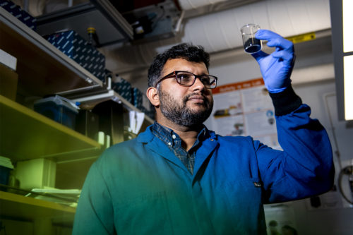 Ameet Pinto, Northeastern assistant professor in civil and environmental engineering, studies how to make water filtration systems that mimic the way water is filtered naturally by manipulating the microbial ecosystems. Here Pinto holds a beaker of activated charcoal, one of the particles he adds to water to absorb contaminants. Photo by Ruby Wallau/Northeastern University