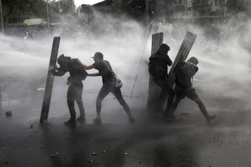 Anti-government demonstrators brace themselves behind shields as they're sprayed with a police water cannon in Santiago, Chile, Tuesday, Oct. 22, 2019. Unrest began last week when a rise in subway fares led to student protests, but then spread nationwide, fueled by frustration among many Chileans who feel they have note shared in the economic advances in one of Latin America’s wealthiest nations. (AP Photo/Rodrigo Abd)