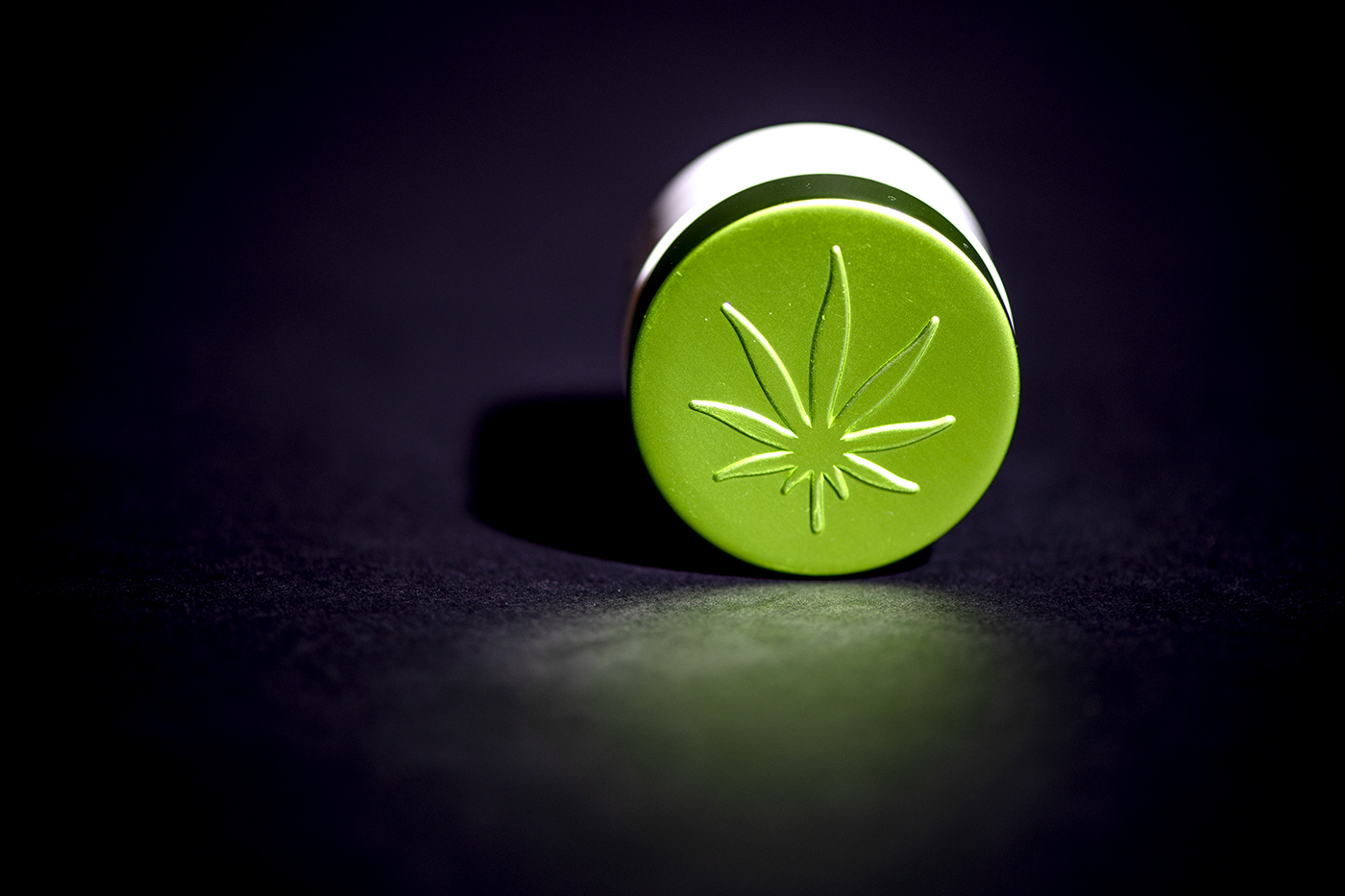 A closeup of a small green tablet with a marijuana leaf on it