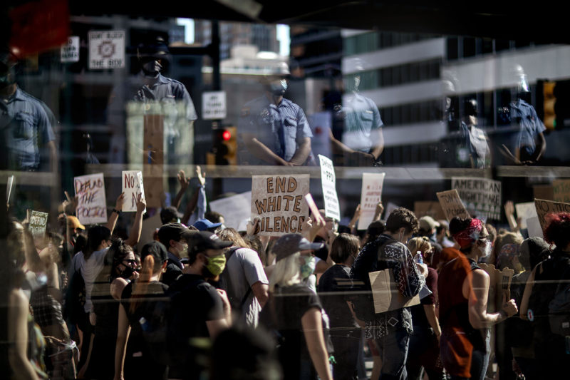 Police officers are reflected in the glass wall of a bus stop as a demonstration calling for the defunding of the police department marches by on June 13, 2020 in Philadelphia. AP Photo/David Goldman