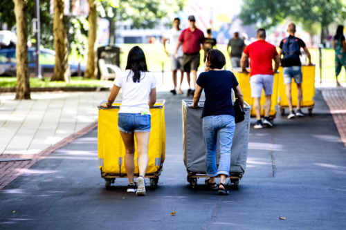 Students walking on campus with moving bins.
