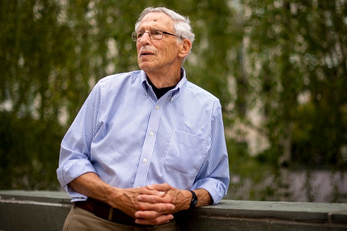 Michael Meltsner, George J. and Kathleen Waters Matthews Distinguished University Professor at Northeastern, leans against a low stone wall outdoors with his hands clasped, looking off to the side.