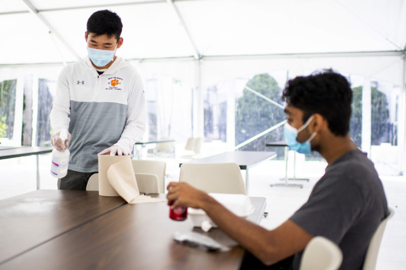 Northeastern student SeungYeop Kang, left, disinfects a table before eating with Deev Patel inside the outdoor dining tent by Speare Hall. Photo by Ruby Wallau/Northeastern University