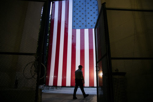 A security guard walks past a giant American flag hanging in Woodrow Wilson Plaza behind temporary metal fencing ahead of the 2020 Republican National Convention, in Washington, D.C., on August 21, 2020 amid the COVID-19 pandemic. AP photo by Graeme Sloan/Sipa USA