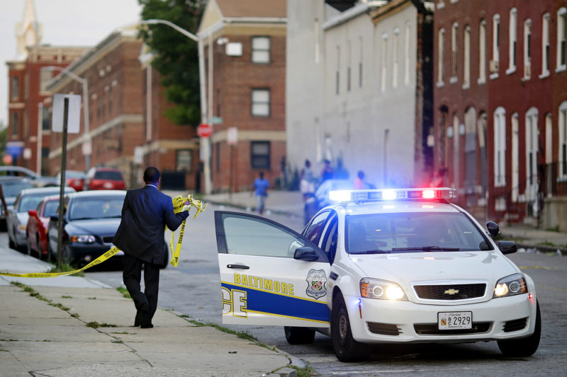 A member of the Baltimore Police Department removes crime scene tape from a corner where a victim of a shooting was discovered in Baltimore on July 30, 2015. AP Photo by Patrick Semansky