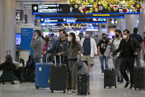 Travelers wearing protective face masks walk through Concourse D at Miami International Airport, Monday, Dec. 28, 2020, in Miami. With the coronavirus surging, the nation's top public health agency asked Americans not to travel and not to spend the holidays with people from outside their household. David Santiago/Miami Herald via AP
