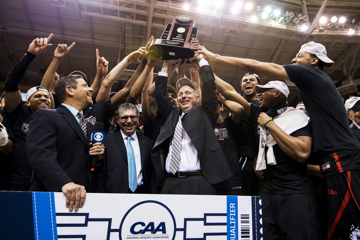Bill Coen raising the CAA trophy, surrounded by players and reporters