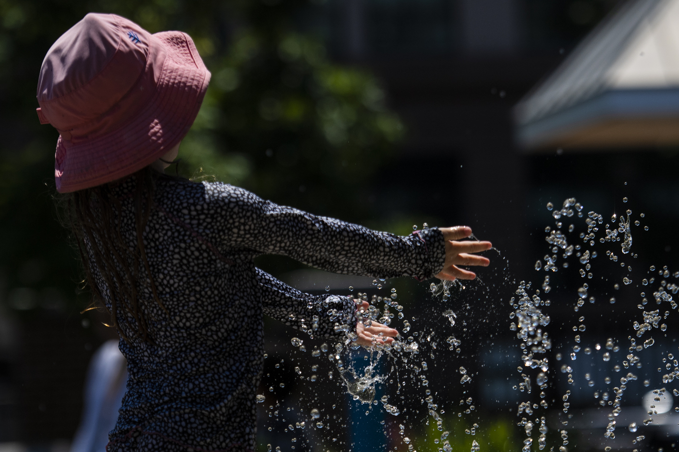 person wearing pink bucket hat playing in a sprinkler