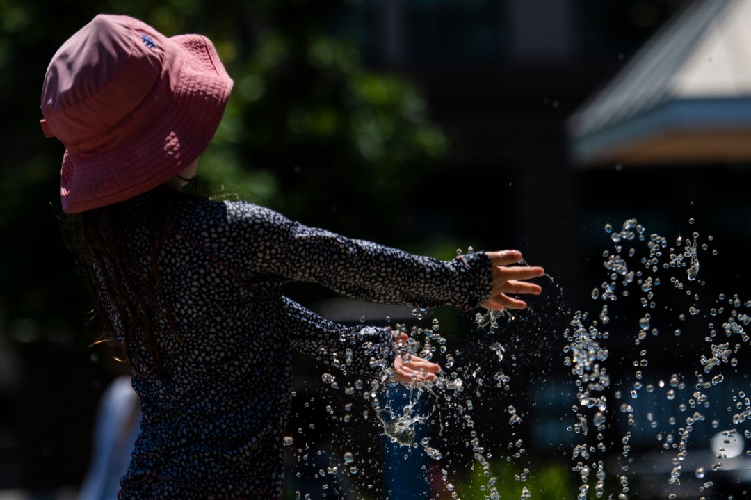 person wearing pink bucket hat playing in a sprinkler
