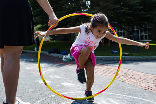 A child in the World Detectives summer program leaps through a hula-hoop during an outdoor break from their reading lessons. Photo by Alyssa Stone/Northeastern University