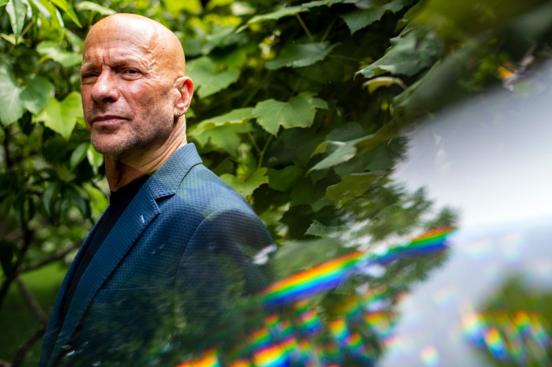 Portrait of Dan Lebowitz wearing a blazer and standing amongst green foliage. 
