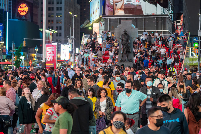 Large crowds of people with and without masks fill Times Square in New York City.
