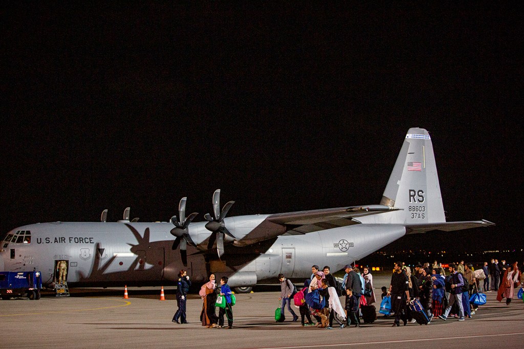 Families evacuated from Afghanistan walk past a U.S Air Force plane that carried them to Kosovo's Pristina International Airport.