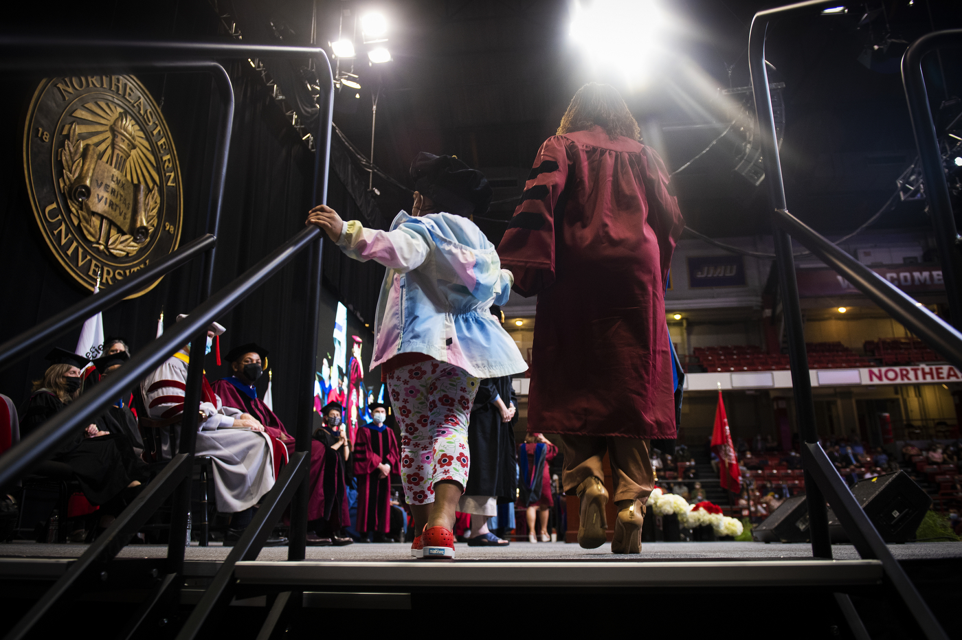 northeastern doctoral graduate crosses stage holding hands with her daughter