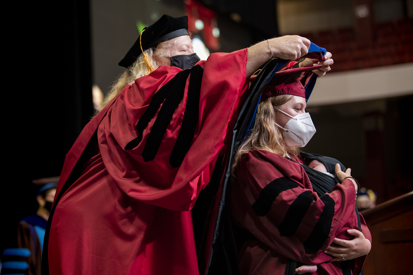 northeastern doctoral graduate holds her baby daughter to her chest while receiving their hood