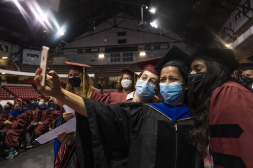 masked northeastern doctoral graduates taking a selfie at hooding ceremony