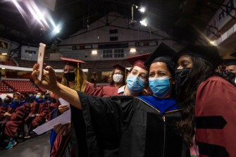 masked northeastern doctoral graduates taking a selfie at hooding ceremony