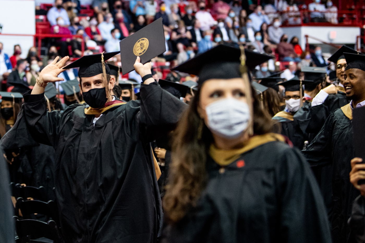 masked northeastern graduate raises his hands in celebration