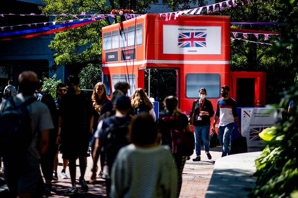 students walking by london red bus replica on northeastern campus