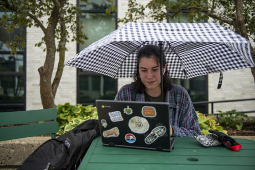 northeastern student using laptop while holding umbrella