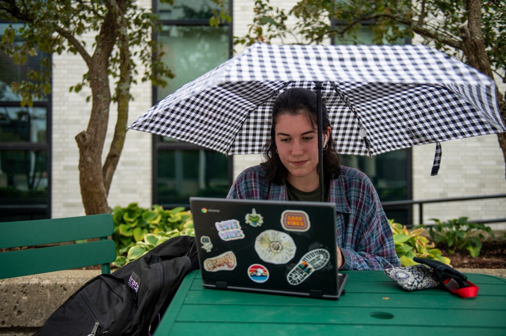northeastern student using laptop while holding umbrella
