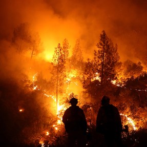 silhouettes of two firefighters standing in front of massive wilfdire