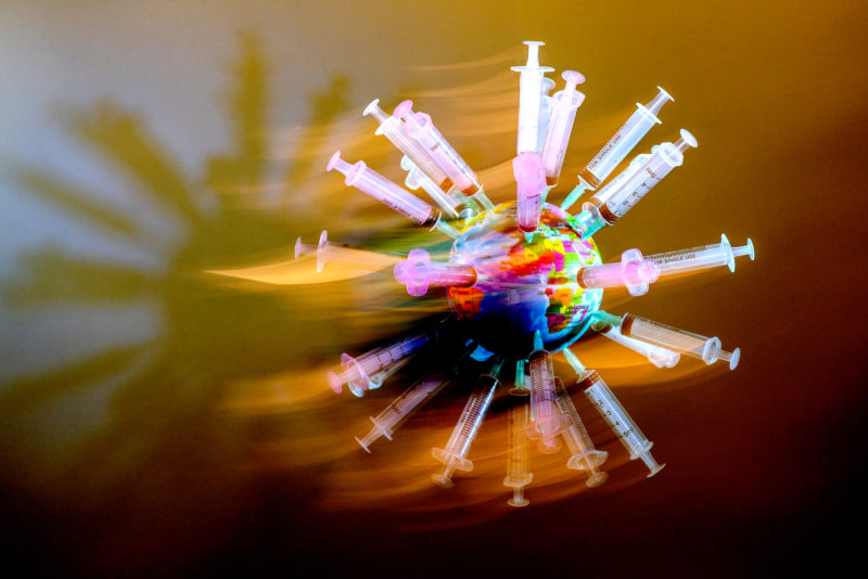 neon syringes stuck into a model globe