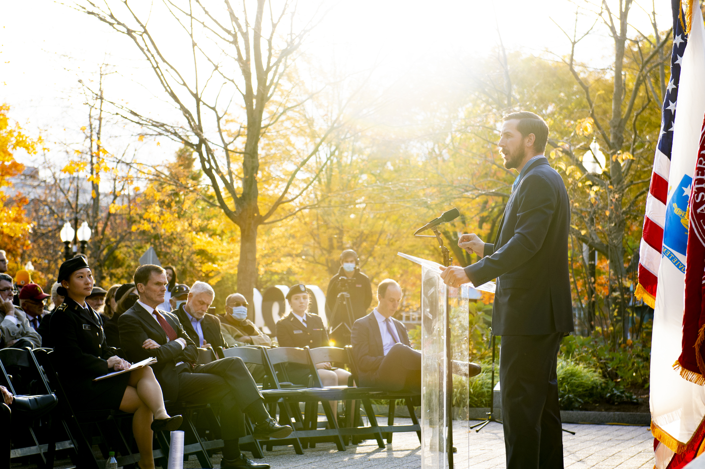 man in suit and tie stands at podium speaking to an audience