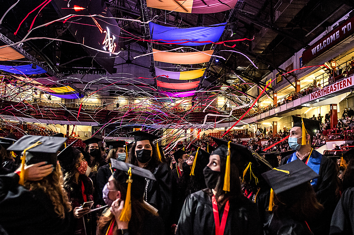 Graduates look up at streamers and brightly colored flags overhead
