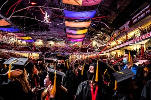 Graduates look up at streamers and brightly colored flags overhead