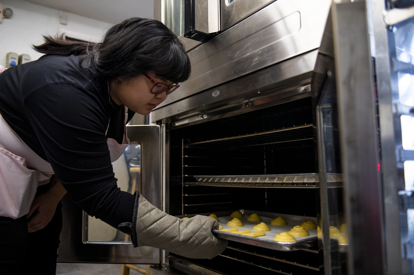 woman putting a tray of yellow sweets into an oven