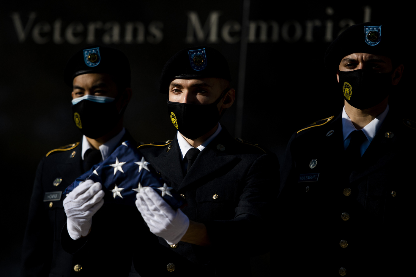 three masked rotc members in uniform one holding folded us flag in front of him