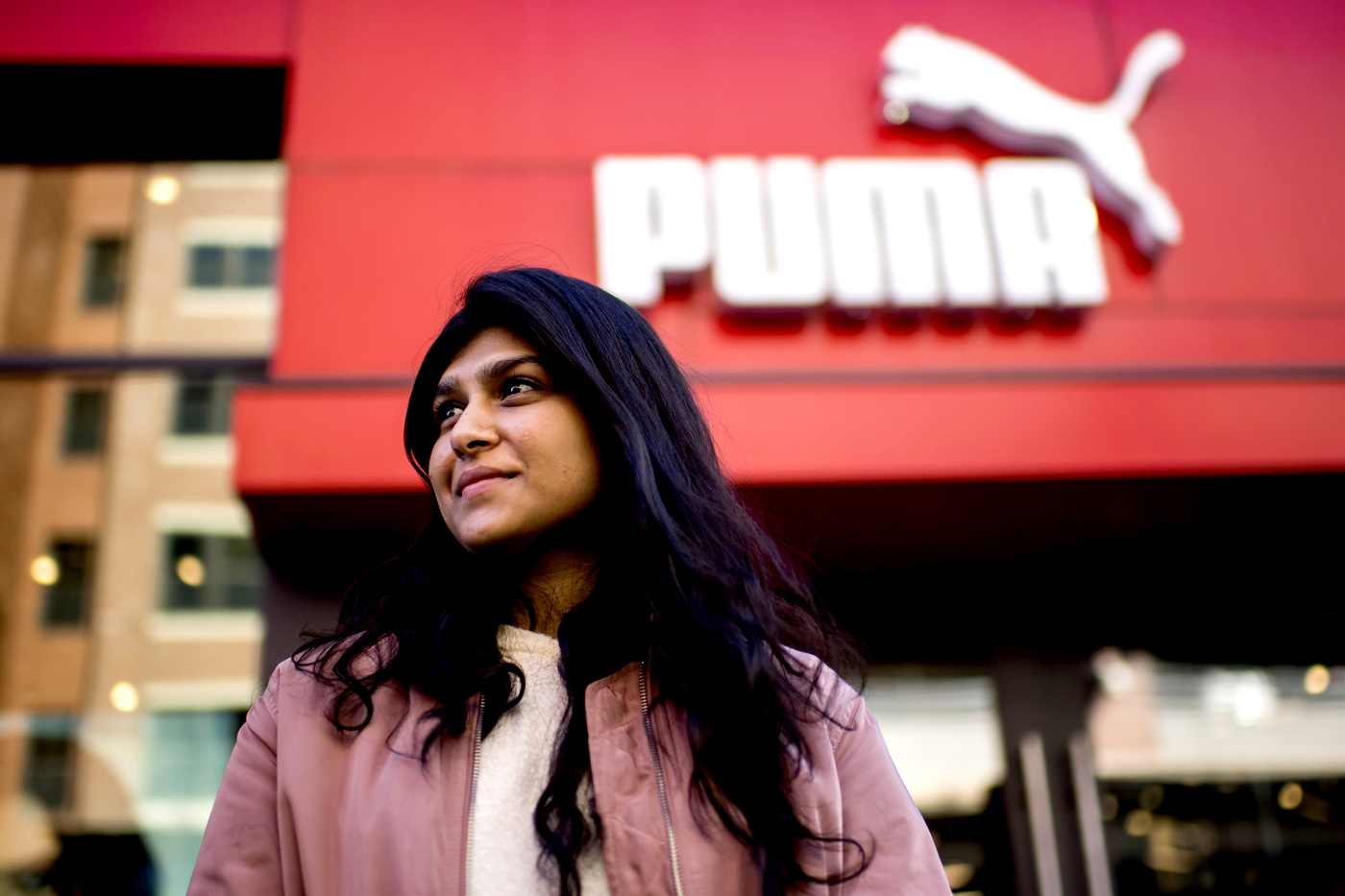 young woman with long dark hair stands in front of puma headquarters 