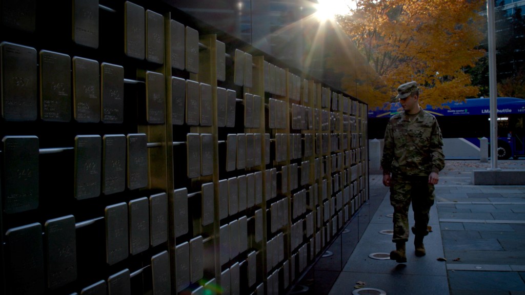 rotc member in uniform walking in front of a wall of memorial plaques
