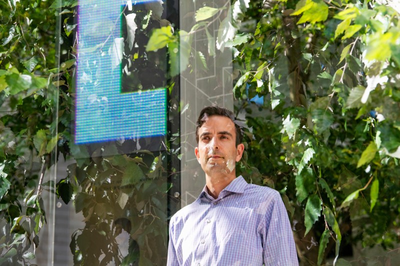 Portrait of Jacob Glickel standing in front of a glass structure with a blue digital display on it. 