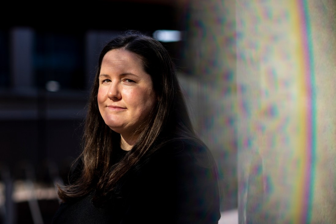 A woman with brown hair dressed in black stands slightly aslant, smiling.