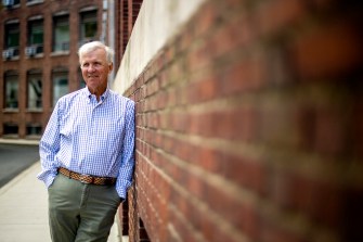 man with white hair leaning against brick wall