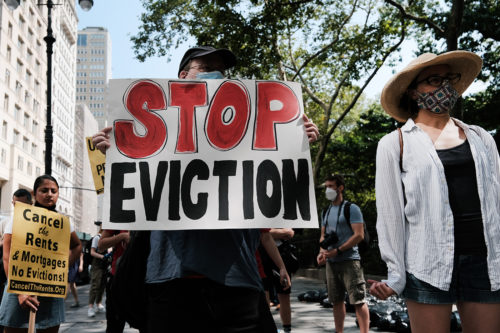masked protester holds a stop eviction sign