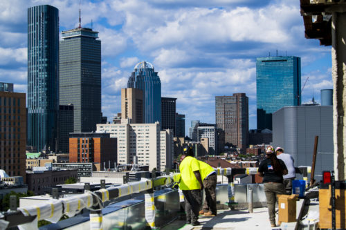 members of the northeastern community stand on the roof of the exp building with downtown boston in the background