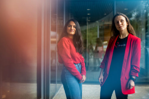 Two women in red tops stand comfortably