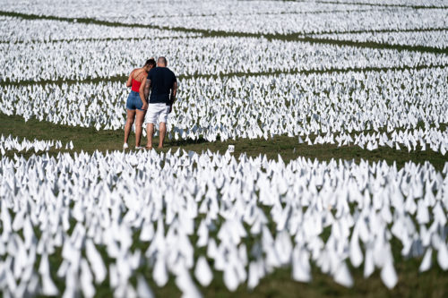 People visit the 'In America: Remember' public art installation near the Washington Monument on the National Mall in Washington, DC. The installation commemorates all the Americans who have died due to COVID-19, a concept by artist Suzanne Brennan Firstenberg, includes more than 650,000 small plastic flags, some with personal messages to those who have died, planted in 20 acres of the National Mall.  Kent Nishimura / Los Angeles Times via Getty Images