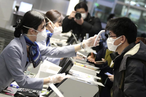A Chinese passenger is checked body temperature by staff wearing mask and rubber glove at the Spring Airlines check-in counter to board an airplane bound for Wuhan at Haneda International Airport in Tokyo on January 31, 2020.  The Yomiuri Shimbun via AP Images 