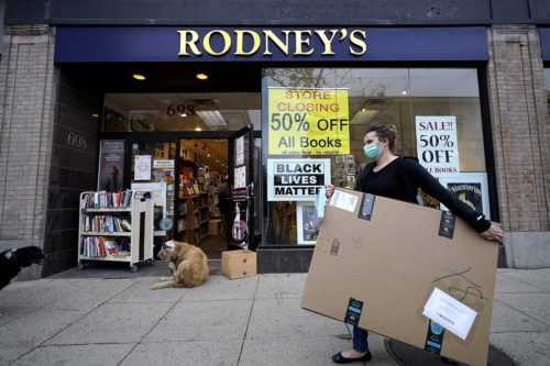 A passer-by carries a box while walking past a bookstore that displays store closing signs on Oct. 26, 2020, in Cambridge, Mass. AP Photo by Steven Senne