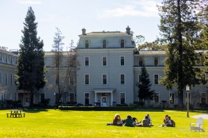 A large white building with green lawn and pine trees in front of it.